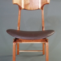 The curvy back rest is "coopered" - which means it is a number of thick wooden pieces whose edges are mitered and then glued to create a wide curve the way coopers used to make barrels. The "racing stripe" effect comes from coopering two sapwood edges so that it looks as though the sapwood - which is white - grew straight up through the center of the tree, and not only along the outside.